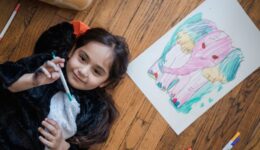Young girl lying on floor drawing a colorful elephant with markers. Creative and fun activity for kids.