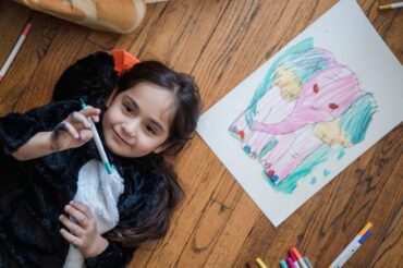 Young girl lying on floor drawing a colorful elephant with markers. Creative and fun activity for kids.