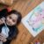 Young girl lying on floor drawing a colorful elephant with markers. Creative and fun activity for kids.